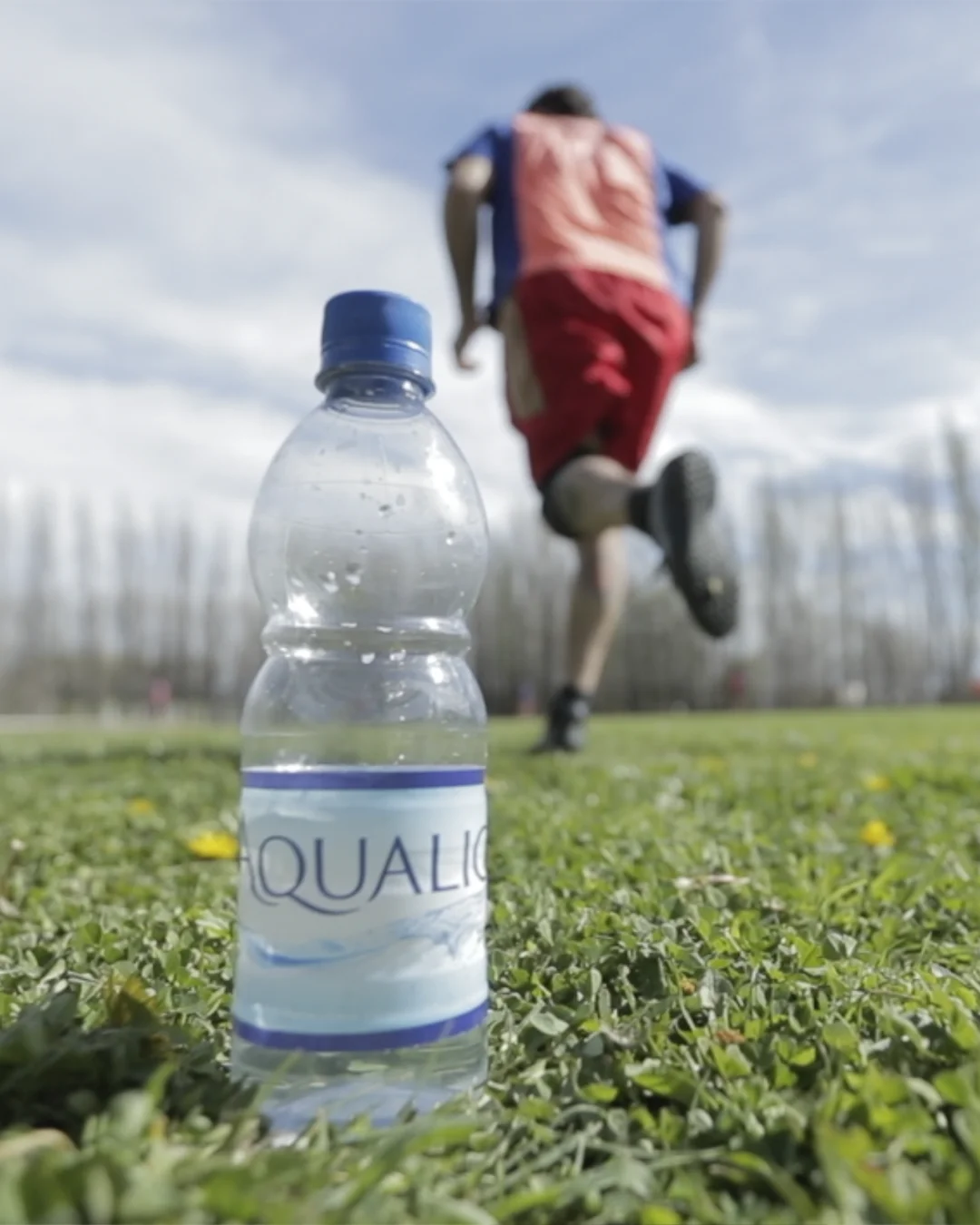 botella 500ml aqualic en campo con jugador de futbol vertical